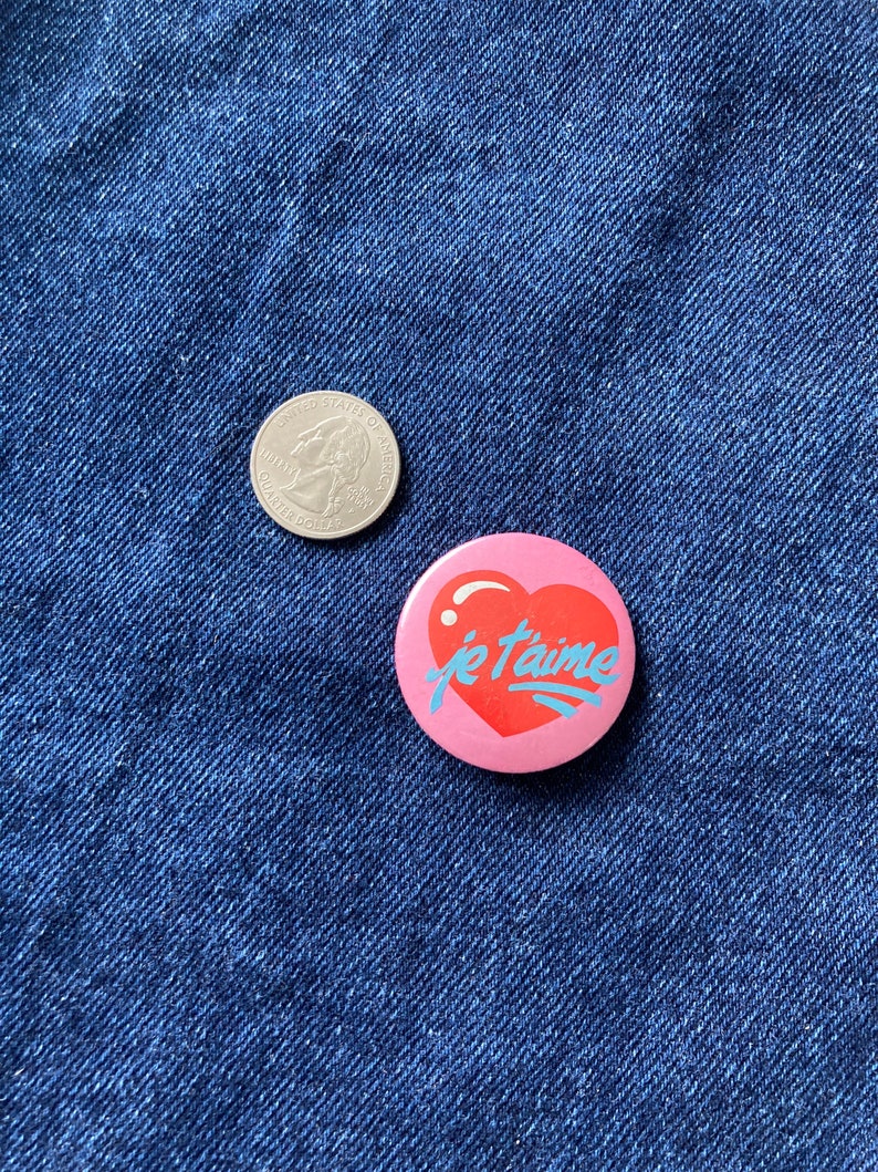 May include: A pink heart-shaped button with the text "je t'aime" in blue lettering.