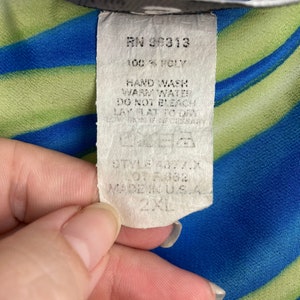 May include: A white tag with black text attached to a blue and green striped fabric. The tag reads "RN 36313 100% POLY HAND WASH WARM WATER DO NOT BLEACH LAY FLAT TO DRY STYLE 4877.X LOT F362 MADE IN USA 2XL".