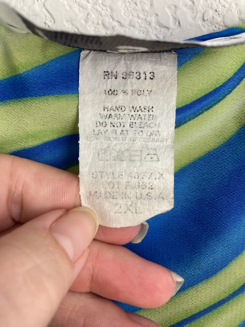 May include: A white tag with black text attached to a blue and green striped fabric. The tag reads "RN 36313 100% POLY HAND WASH WARM WATER DO NOT BLEACH LAY FLAT TO DRY STYLE 4877.X LOT F362 MADE IN USA 2XL".