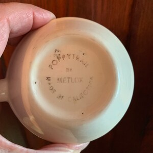 May include: The bottom of a white ceramic cup with the words "Poppytrail by Metlox Made in California" printed on it.