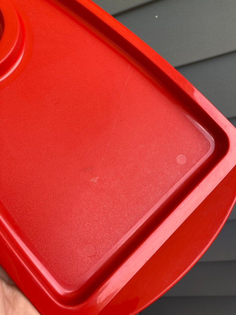 May include: A bright red plastic container lid with a slightly rounded edge. The lid has a smooth surface with a few scratches.