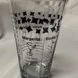 Puede incluir: Un vaso medidor de vidrio transparente con dise&ntilde;os de estrellas negras e instrucciones para hacer una margarita y un bloody mary. La receta de la margarita requiere 3 cl de tequila, 1 cl de triple sec y 1 cl de jugo de lim&oacute;n. La receta del bloody mary requiere 3 cl de vodka, 6 cl de jugo de tomate, 1 cucharadita de salsa Worcestershire y 1/2 cucharadita de salsa picante.