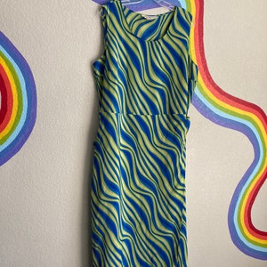 May include: A sleeveless midi dress with a green and blue wavy pattern. The dress has a wrap style and a tie at the waist.