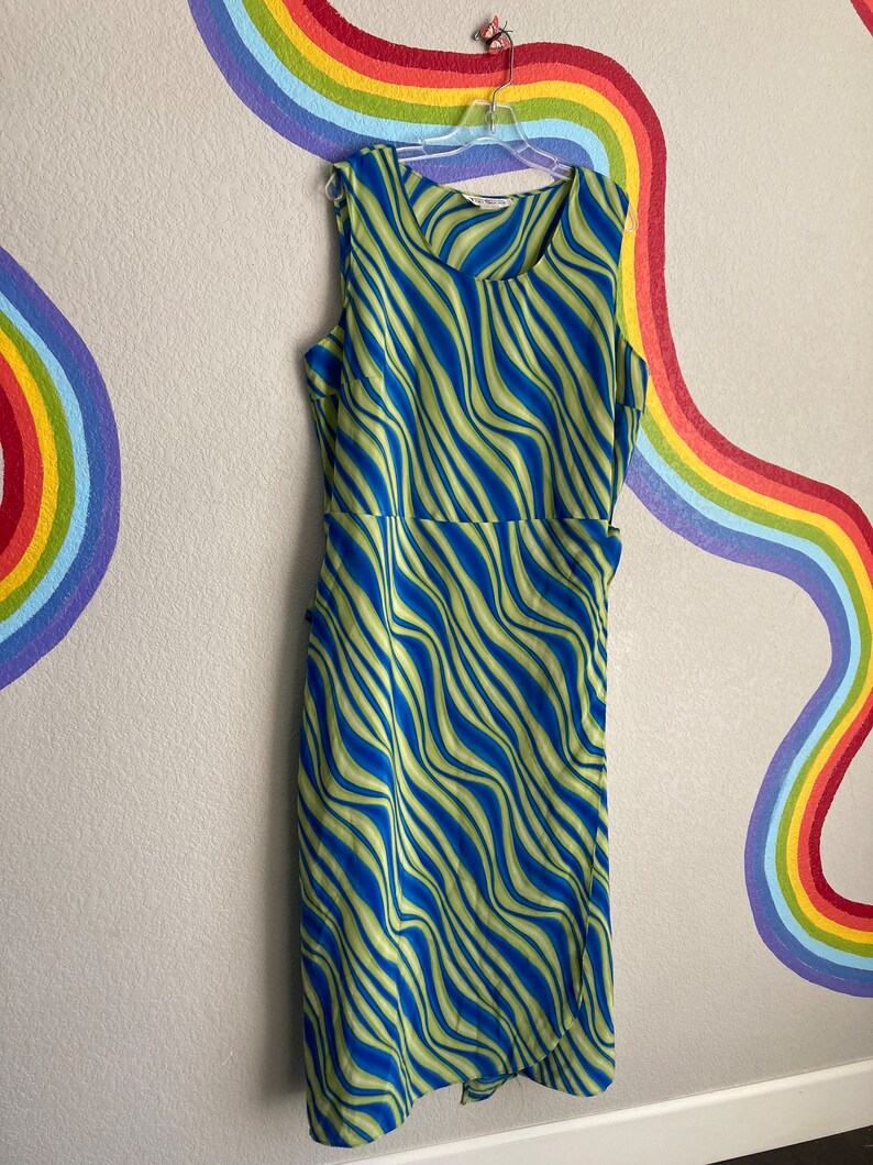 May include: A sleeveless midi dress with a green and blue wavy pattern. The dress has a wrap style and a tie at the waist.