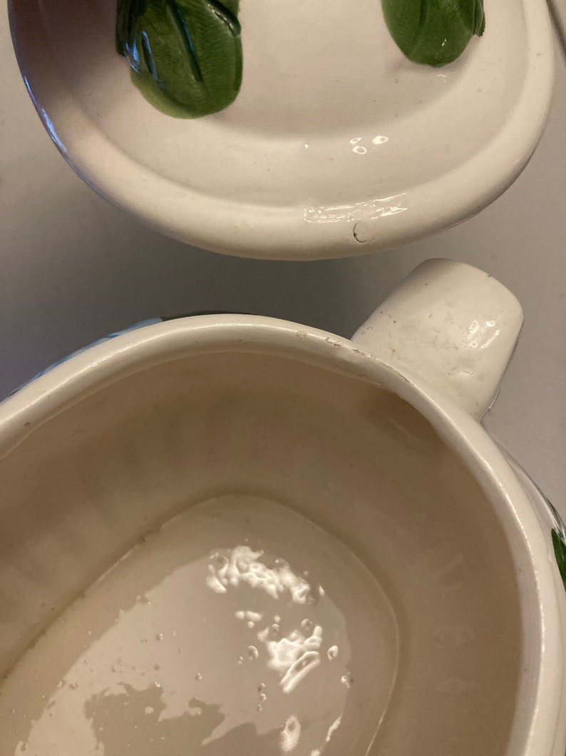 May include: White ceramic serving dish with a green floral design. The dish has a lid with a handle. The dish is empty.