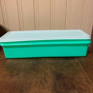 May include: A green plastic rectangular storage container with a white lid. The container is sitting on a wooden surface.