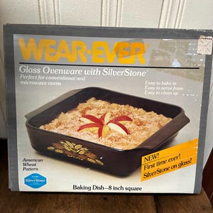 May include: A rectangular black baking dish with a wheat pattern, filled with a baked dessert and apple slices. The box reads "WEAR-EVER" and "Glass Ovenware with SilverStone." The dish is 8 inches square.
