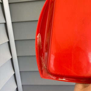 May include: A bright red plastic tray with a slightly curved edge. The tray has a white residue on the edge.