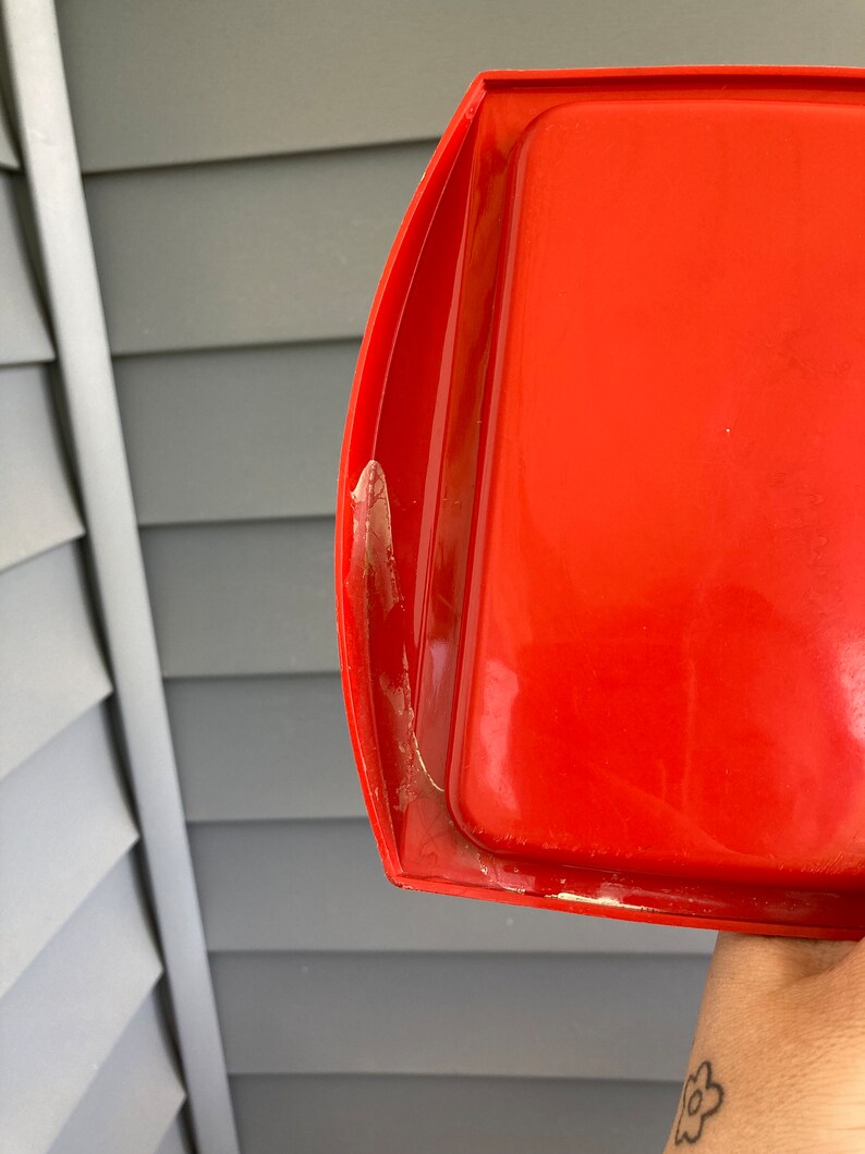 May include: A bright red plastic tray with a slightly curved edge. The tray has a white residue on the edge.