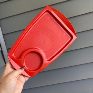 May include: A bright red plastic tray with a small circular indentation. The tray is designed for holding a cup or mug.