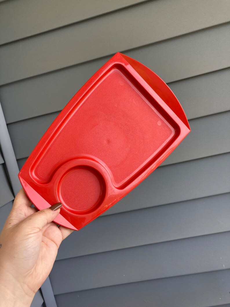 May include: A bright red plastic tray with a small circular indentation. The tray is designed for holding a cup or mug.