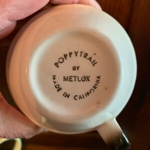 May include: White ceramic cup with a black and white logo that reads "Poppytrail by Metlox Made in California".