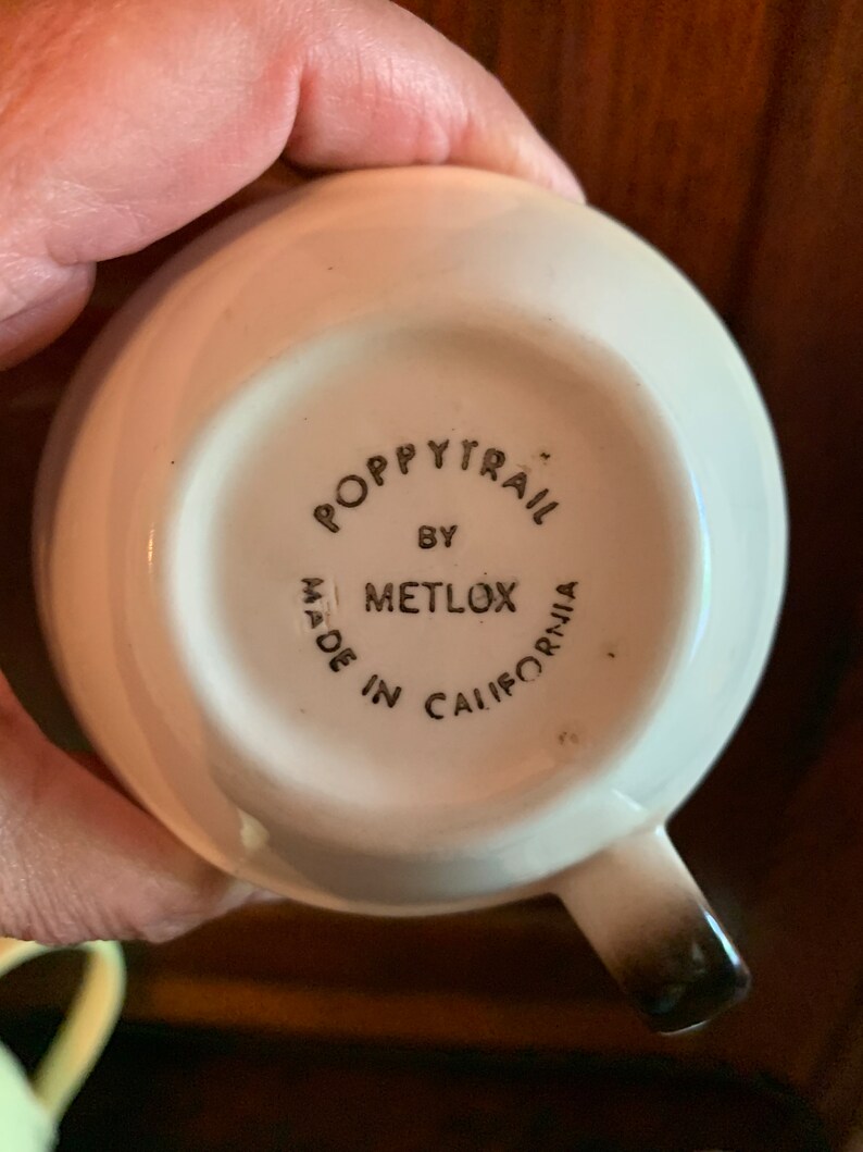 May include: White ceramic cup with a black and white logo that reads "Poppytrail by Metlox Made in California".