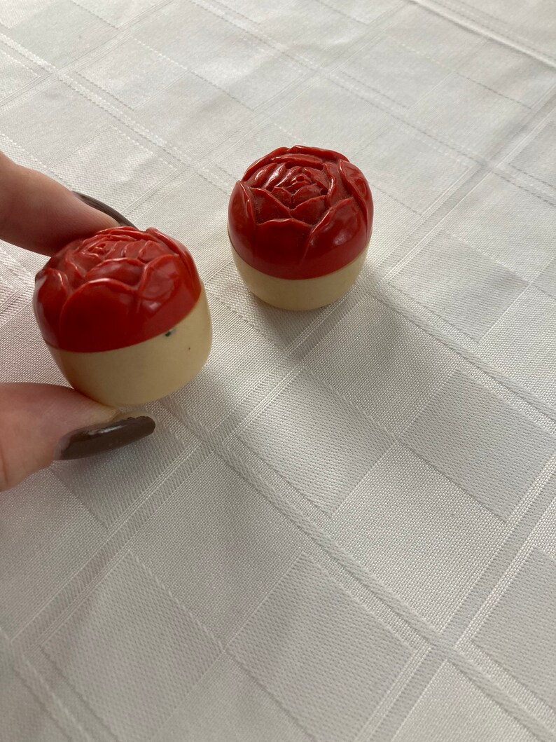 May include: Two small, round, red and white containers with a rose design on the top. The containers are made of plastic.