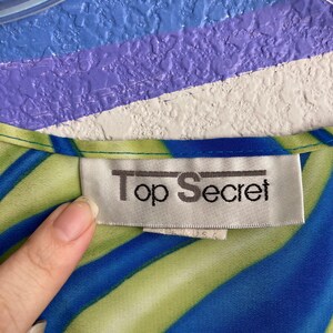 May include: A blue and green striped shirt with a white tag that says "Top Secret" on it.