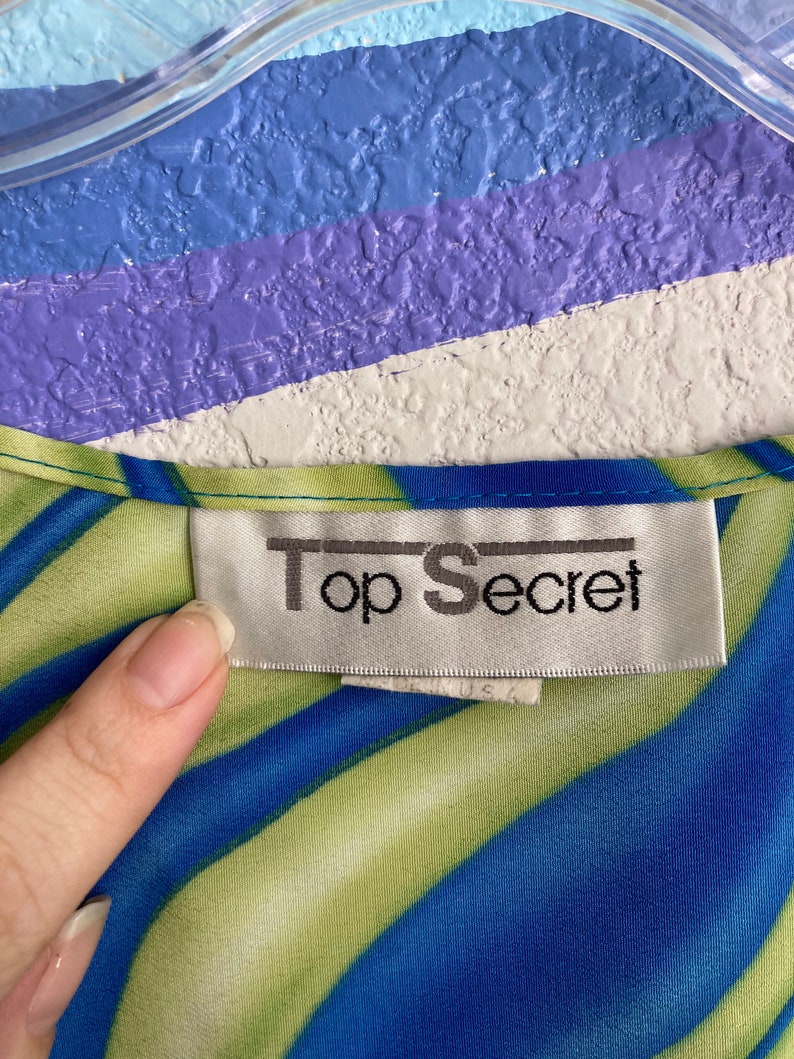 May include: A blue and green striped shirt with a white tag that says "Top Secret" on it.