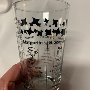 Puede incluir: Un vaso medidor de vidrio transparente con dise&ntilde;os de estrellas negras y medidas para hacer c&oacute;cteles. El vaso tiene recetas para una margarita, un bloody mary y un martini seco.