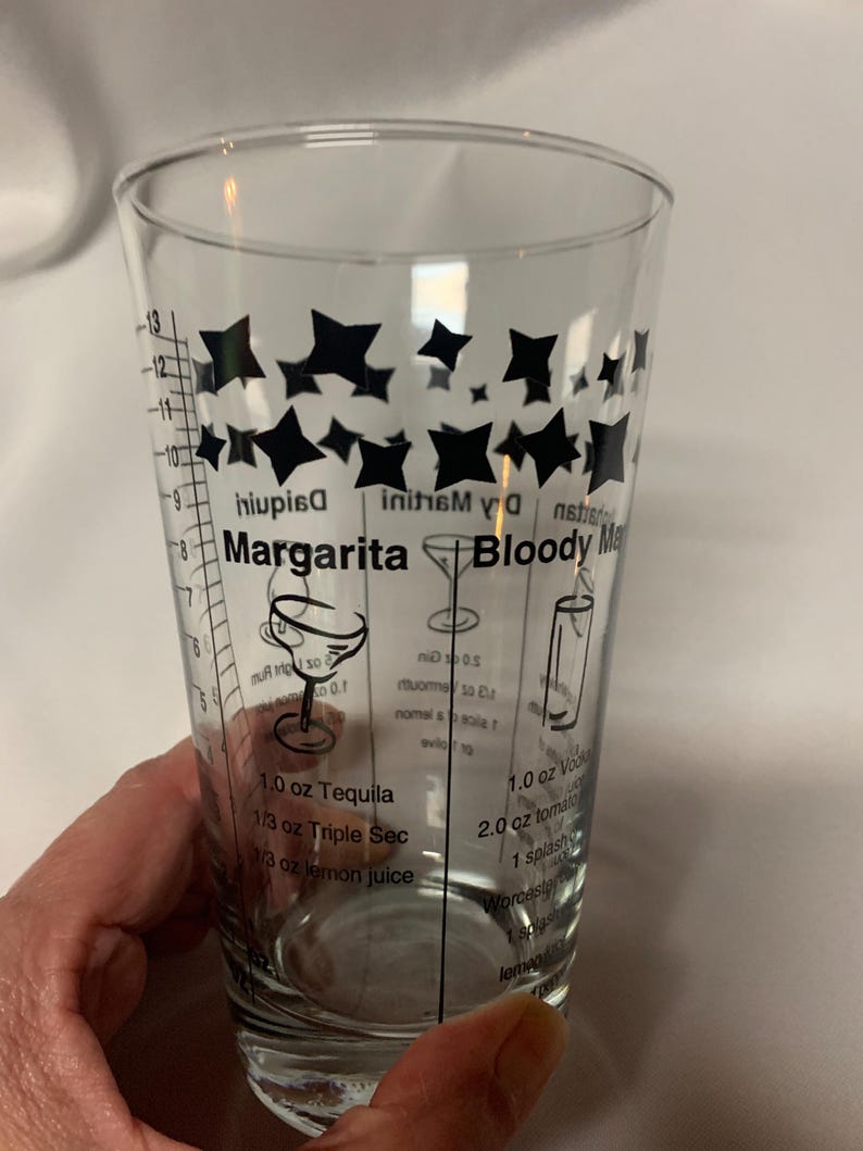 Puede incluir: Un vaso medidor de vidrio transparente con dise&ntilde;os de estrellas negras y medidas para hacer c&oacute;cteles. El vaso tiene recetas para una margarita, un bloody mary y un martini seco.