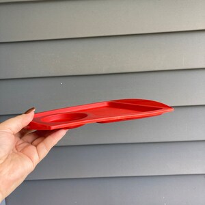 May include: A red plastic tray with two circular indentations, likely for holding cups or glasses.