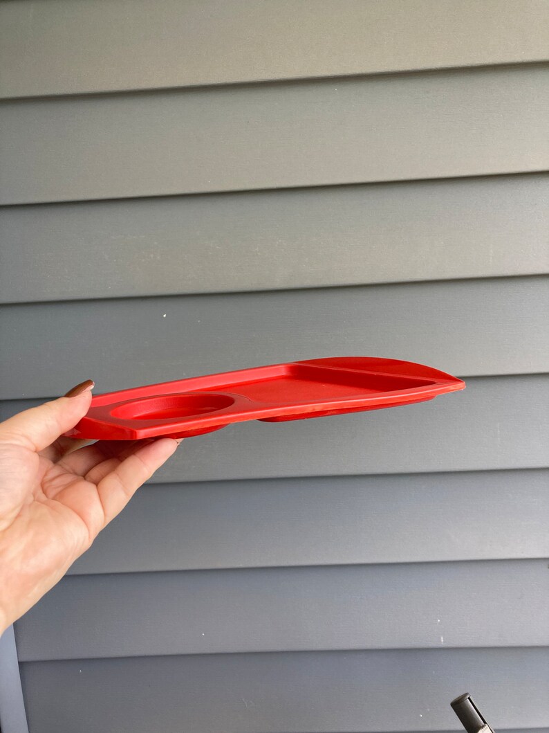 May include: A red plastic tray with two circular indentations, likely for holding cups or glasses.