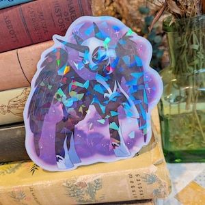 May include: A holographic sticker featuring a dark, winged equine character with a horn, set against a purple background. The sticker has a reflective, shattered-glass effect that displays various colors across the surface of the figure.