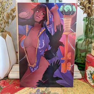 May include: A fantasy art print featuring a dark-skinned woman with green eyes, wearing a purple robe, and surrounded by black ravens. A large key and a glowing orb are also visible. The artwork has a mystical theme.