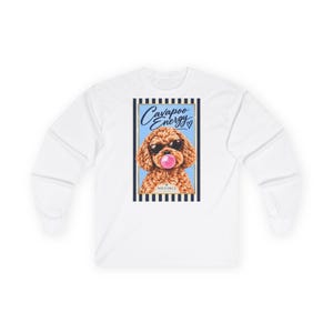 Può includere: Una maglietta bianca a maniche lunghe con una grafica rettangolare di un cane Cavapoo marrone che indossa occhiali da sole neri e soffia una bolla di gomma da masticare rosa. Il testo "Cavapoo Energy" e "NOUS DEUX" appare nella grafica, incorniciato da strisce blu navy.