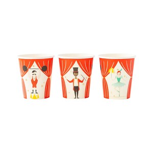 Puede incluir: Tres vasos de papel con diseños de temática circense. Los vasos son blancos con detalles rojos y dorados. Los diseños representan a un hombre fuerte, un mago y una bailarina.