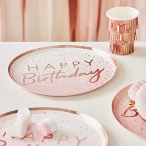 Könnte beinhalten: Rosa und weiße Pappteller mit einem roségoldenen Folienrand und dem Text "Happy Birthday" in roségoldener Folie. Die Teller haben einen dezenten rosafarbenen Ombre-Effekt und weiße Punkte.