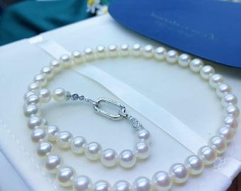 May include: A strand of white, round pearls arranged in a circular pattern. The necklace features a silver-toned, oval-shaped link clasp adorned with small, clear, sparkling stones on each side, connecting the two ends of the pearl strand.