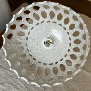 Underside of speckled white ceramic shade laid on linen; oval cutouts create lace-like pattern, central E26 socket shown—close-up of handcrafted openwork pottery lighting.