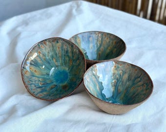 May include: Three ceramic bowls with a blue, green and brown glaze. The bowls are handmade and have a unique, organic look.