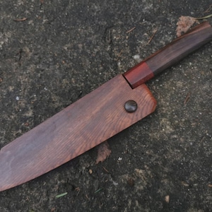 Könnte beinhalten: Ein Holzmesser mit einem dunkelbraunen Griff und einem roten Akzent. Die Klinge ist ebenfalls aus Holz und hat eine natürliche Oberfläche.