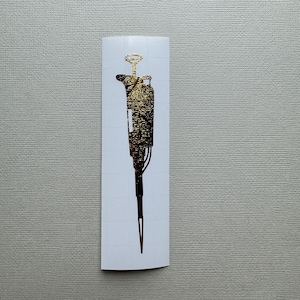 May include: A gold-colored pipette sticker. The sticker is on a white background.