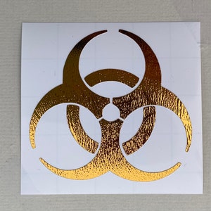May include: Gold biohazard symbol sticker on a white background.