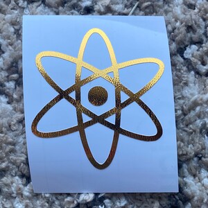 Może przedstawiać: Złota naklejka z symbolem atomu na białym tle.