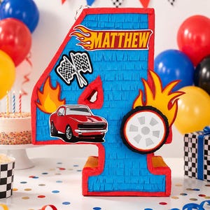 May include: A blue number four piñata with red trim, decorated with a red car, a tyre, flames, and chequered flags. The name MATTHEW is printed in a yellow and orange flame-style font at the top. The piñata features fringed paper texture.