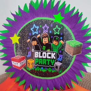 May include: A round piñata featuring a purple and green fringed border and a central graphic with three cartoon characters, the text BLOCK PARTY, a TNT block, a grass block, and a question mark block. Orange streamers hang from the bottom edge.