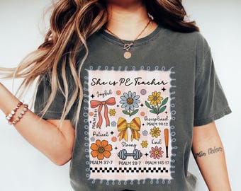 May include: Dark grey t-shirt with a colorful graphic that reads "She is PE Teacher." The design includes flowers, bows, a baseball bat, and the words "Joyful," "Patient," "Strong," "Disciplined," and "Kind."