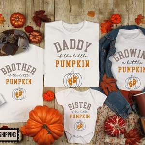 May include: White t-shirts and a onesie with fall-themed text and graphics. The shirts read "Brother of the little Pumpkin", "Daddy of the little Pumpkin", "Growing a little Pumpkin", and "Sister of the little Pumpkin". A large orange pumpkin is in the center.