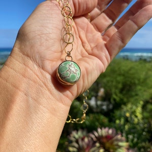 May include: A gold chain necklace with a green and white stone pendant. The pendant is round and has a gold setting.