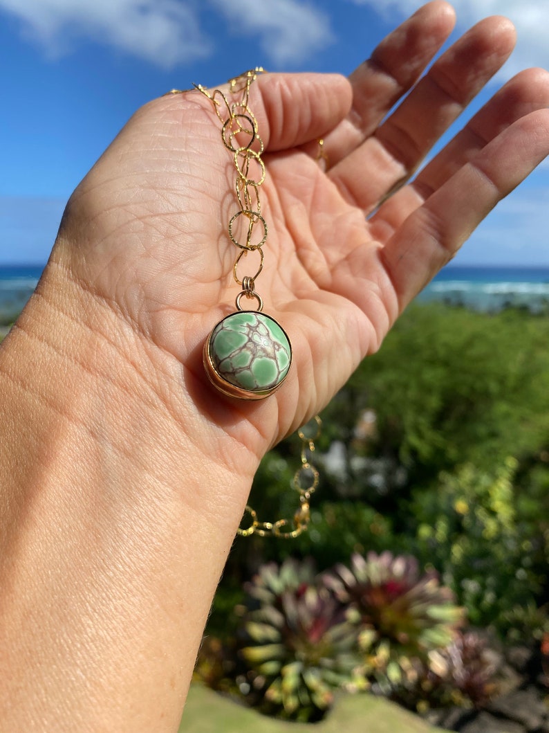 May include: A gold chain necklace with a green and white stone pendant. The pendant is round and has a gold setting.