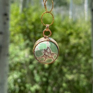May include: A gold chain necklace with a round pendant featuring a green and brown gemstone.