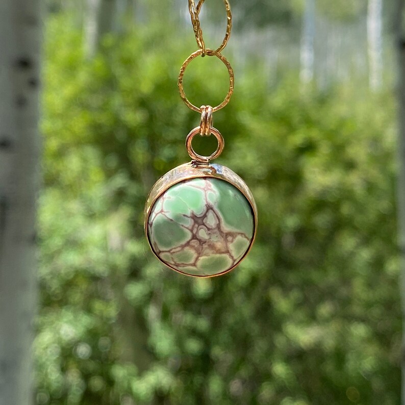 May include: A gold chain necklace with a round pendant featuring a green and brown gemstone.