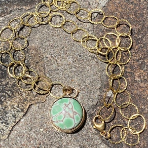 May include: A gold chain necklace with a round green and white stone pendant. The chain is made of small, linked circles.