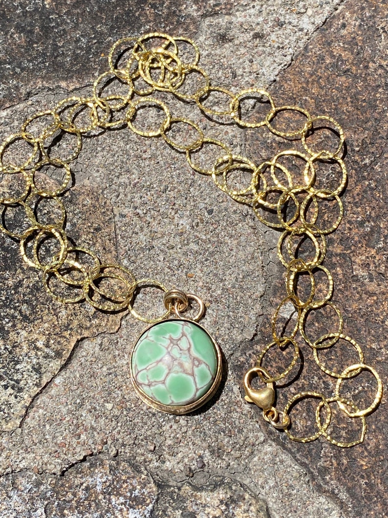 May include: A gold chain necklace with a round green and white stone pendant. The chain is made of small, linked circles.