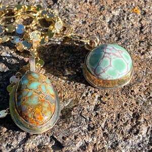 May include: Two gold necklaces with green and brown stone pendants. The stones are set in gold bezels and have a marbled pattern.