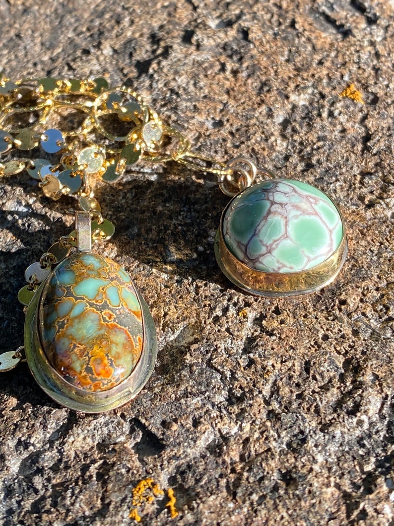 May include: Two gold necklaces with green and brown stone pendants. The stones are set in gold bezels and have a marbled pattern.