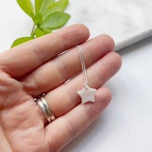 May include: A delicate silver chain necklace with a white star-shaped pendant. The pendant is made of a smooth, white material, possibly mother of pearl.