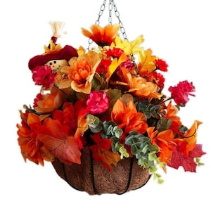 May include: A hanging fall floral arrangement in a coconut fiber basket with a scarecrow figurine. The arrangement features orange, red, and yellow flowers and leaves.